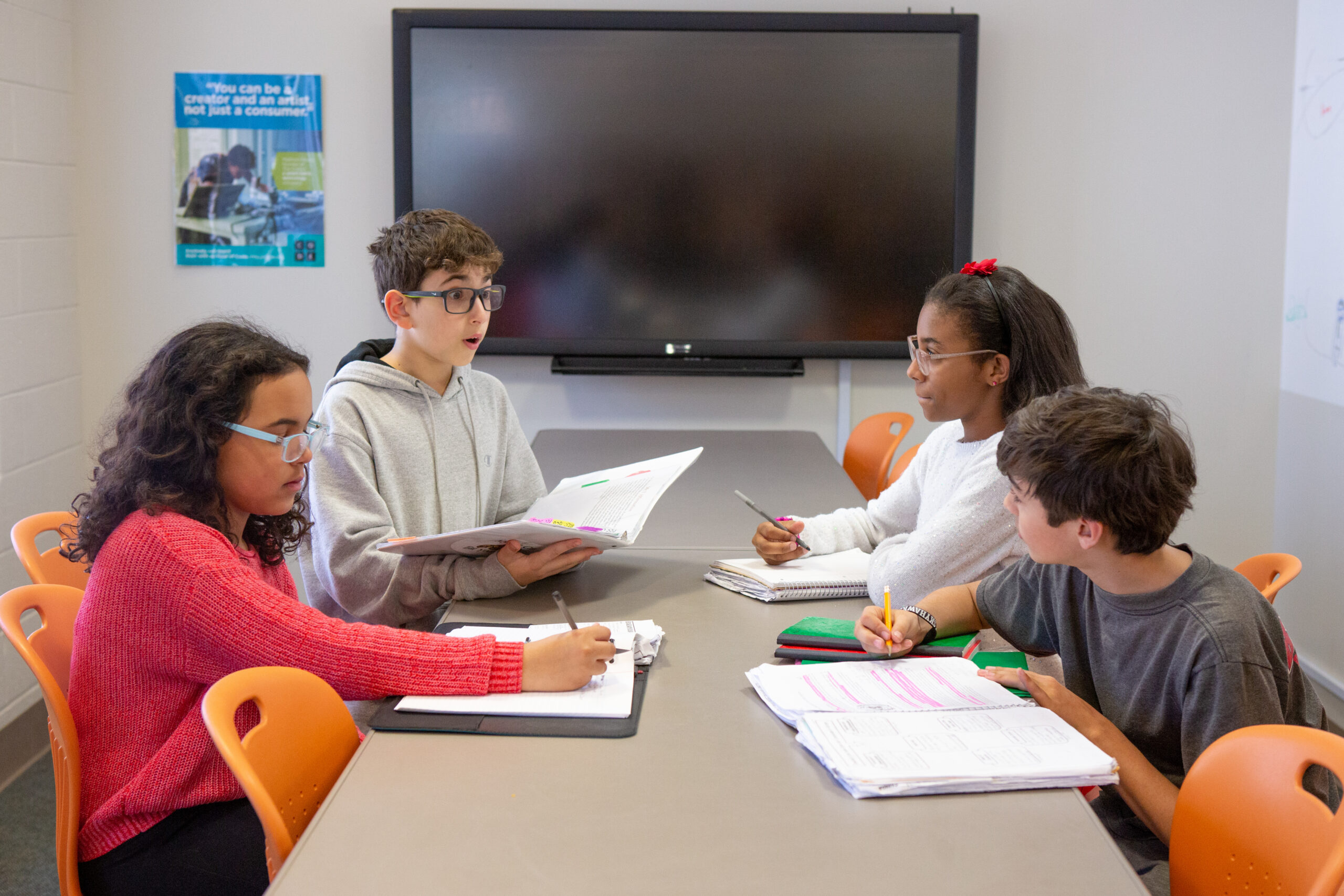 An image of two male middle schoolers and two female middle schoolers working together at a table, with notebooks in front of them