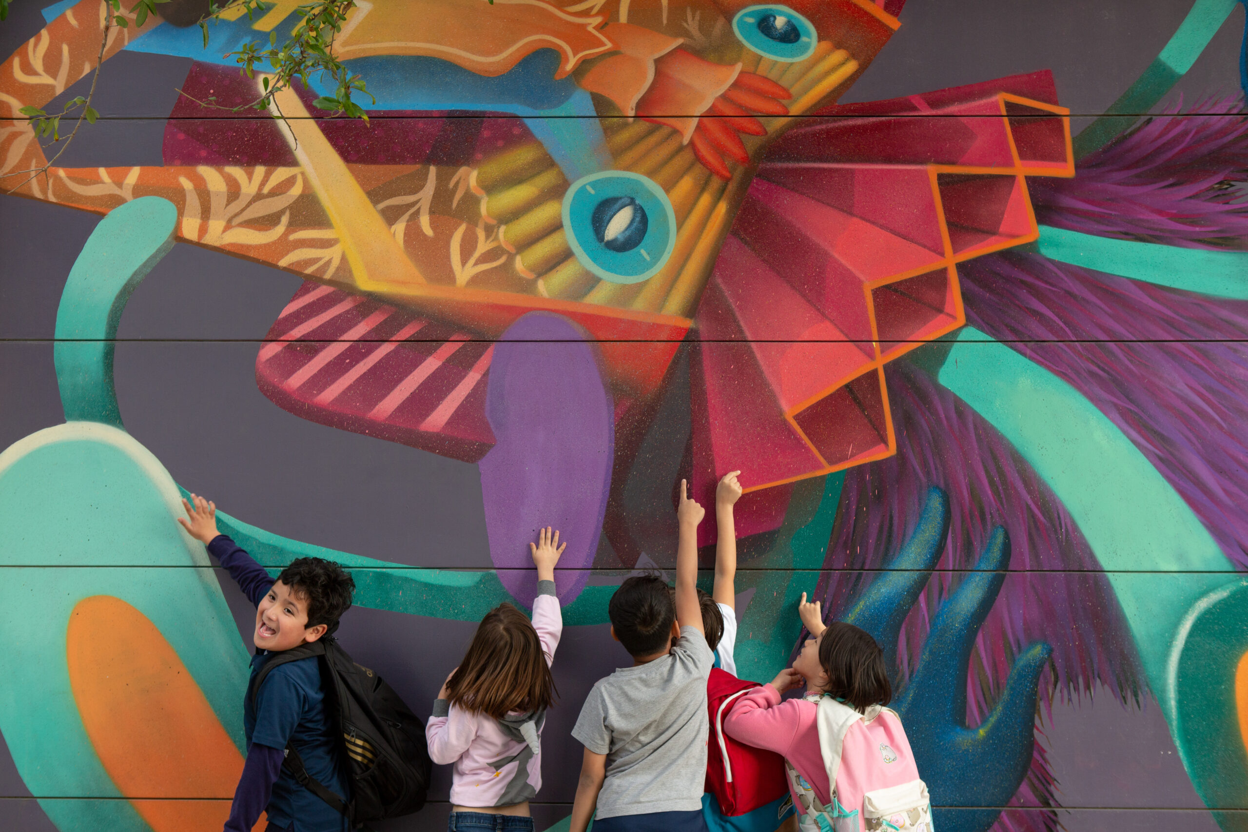 A group of elementary students enjoy a mural on their school campus.