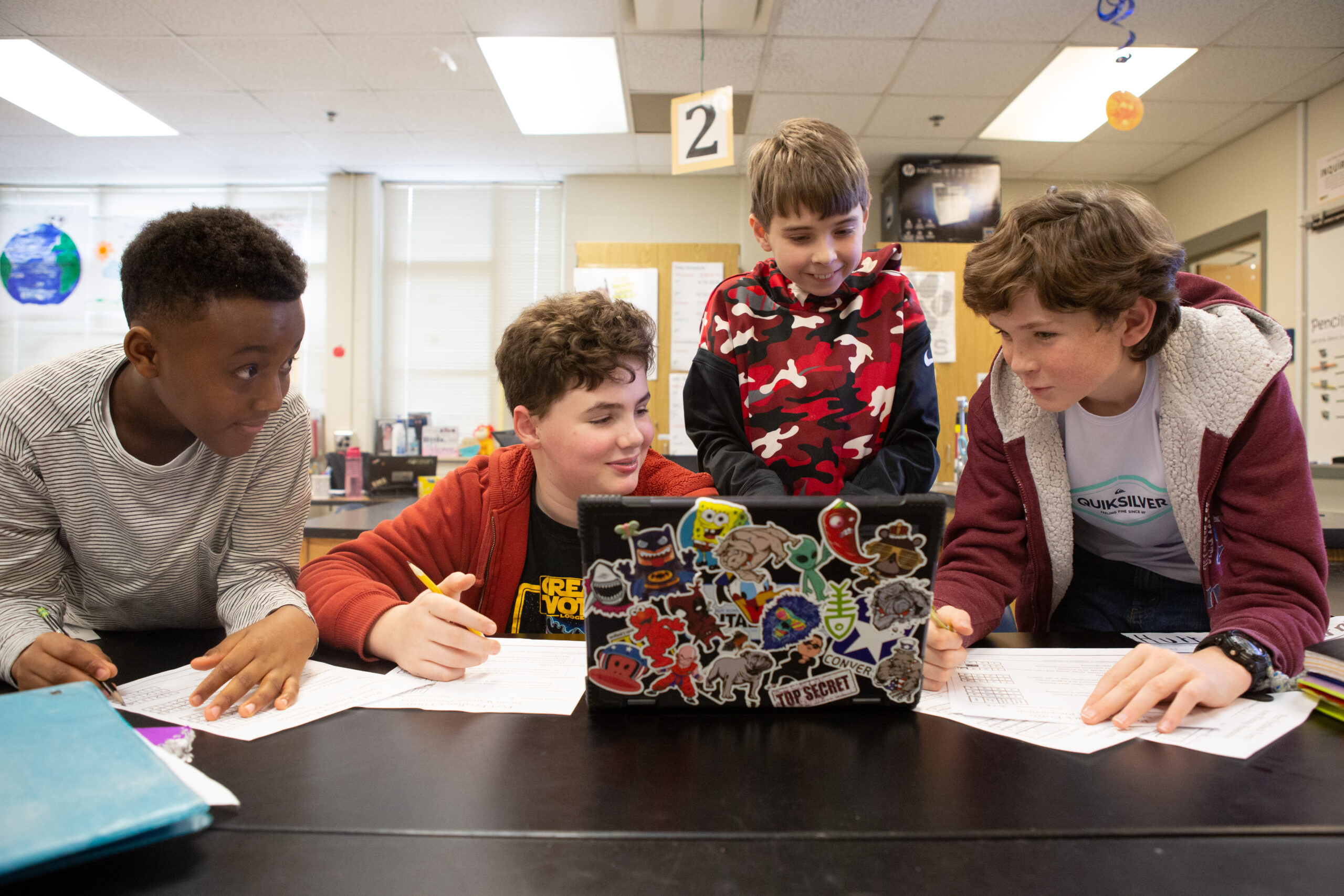 An image of four male sixth-graders sitting around a shared laptop and working together.