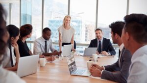 Businesswoman Stands To Address Meeting Around Board Table