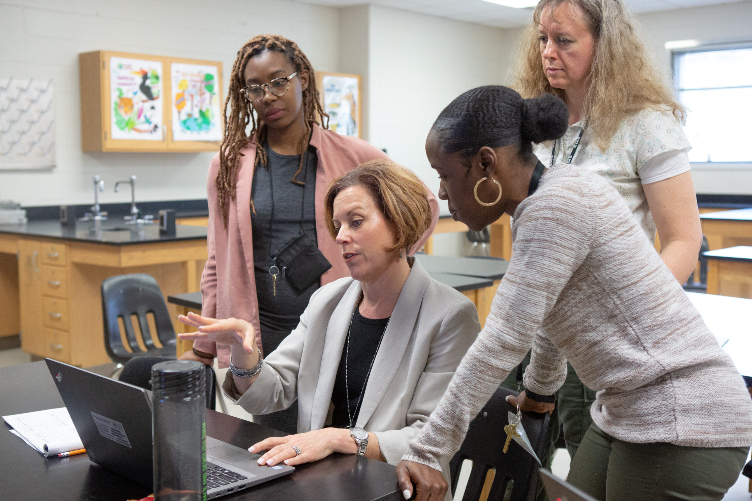 Middle school science teachers sit around a laptop and discuss their lesson plan