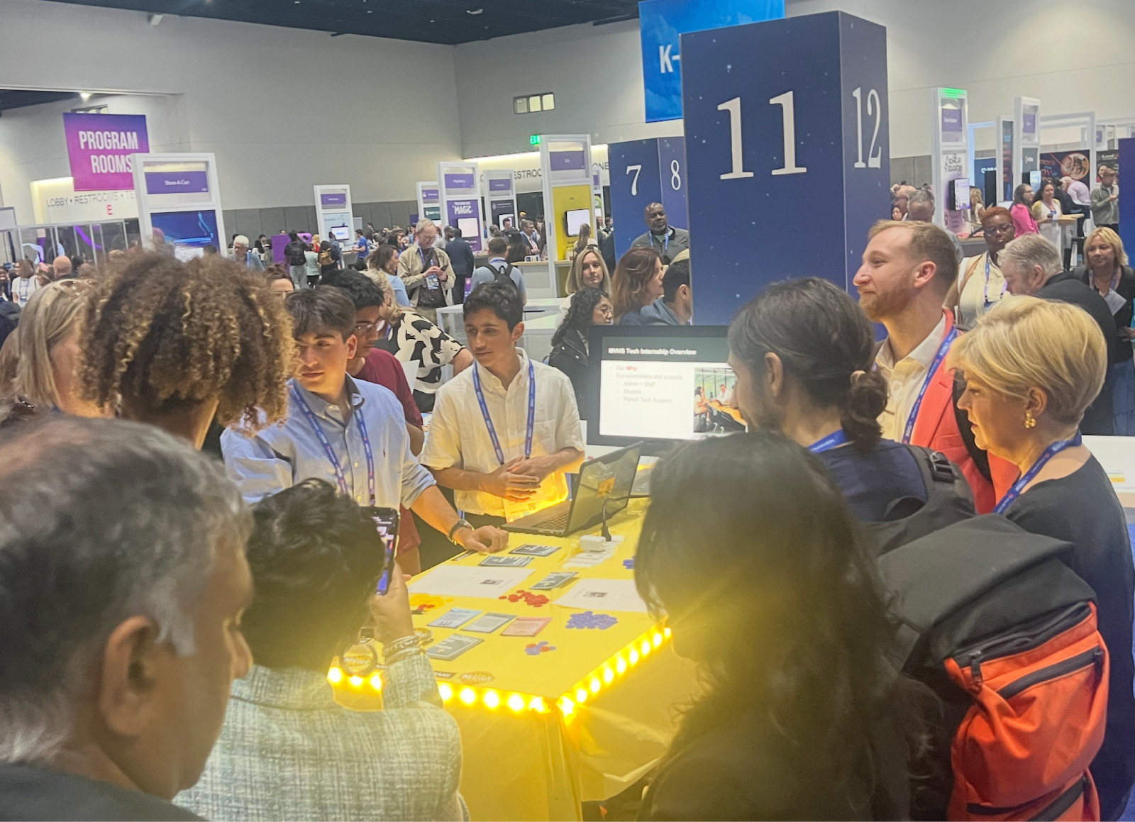 Students and adults stand around a table at a conference booth to showcase the items on display.
