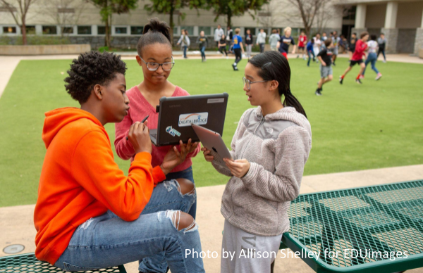 Three eighth-grade students work together on an assignment in a school courtyard.